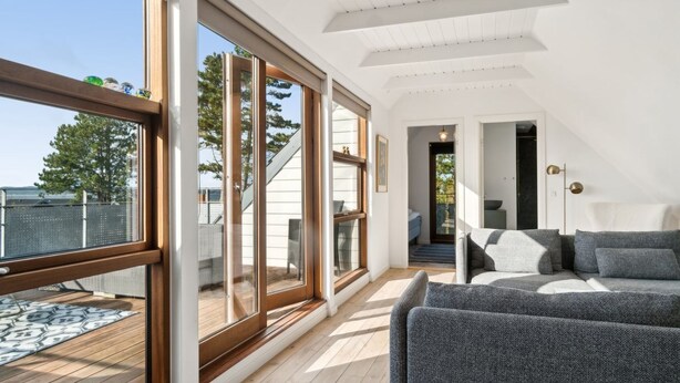Une pièce spacieuse dotée de grandes fenêtres, d’une terrasse en bois et d’un canapé moderne.