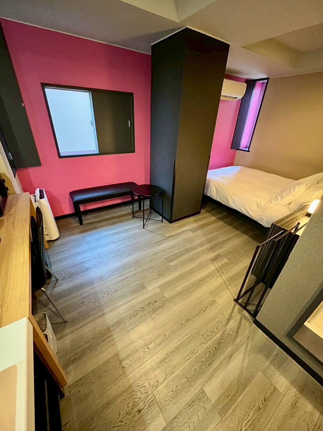 A compact room with a wooden floor, a bed, a bench, and a desk.
