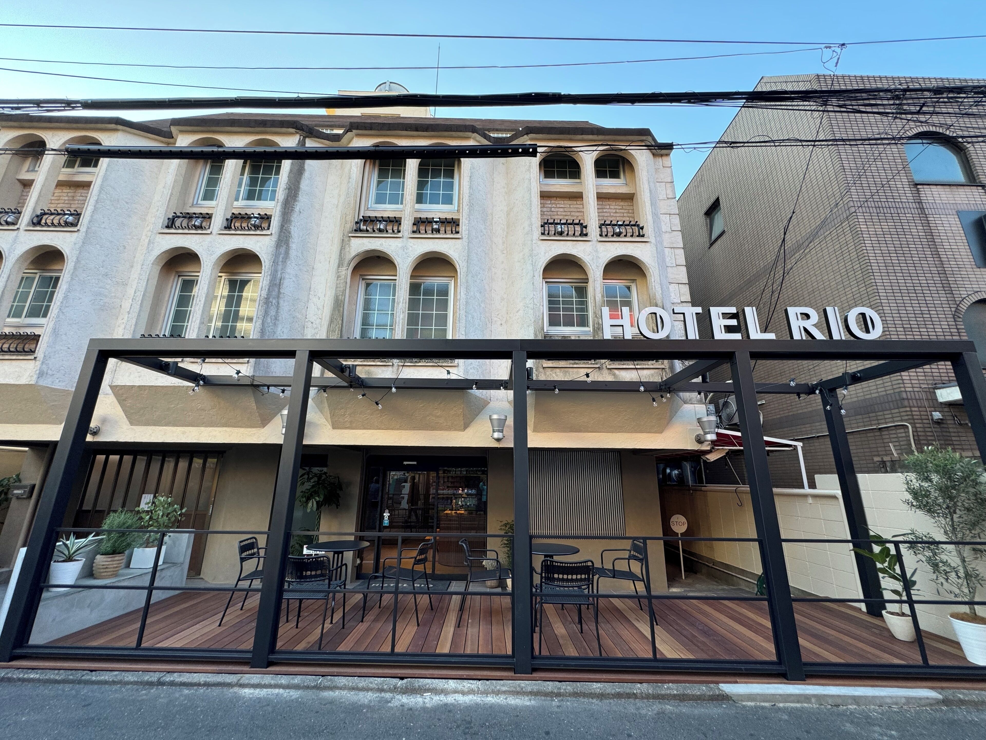 A hotel named HOTEL RIO with a modern entrance, outdoor seating area, and a classic building facade.