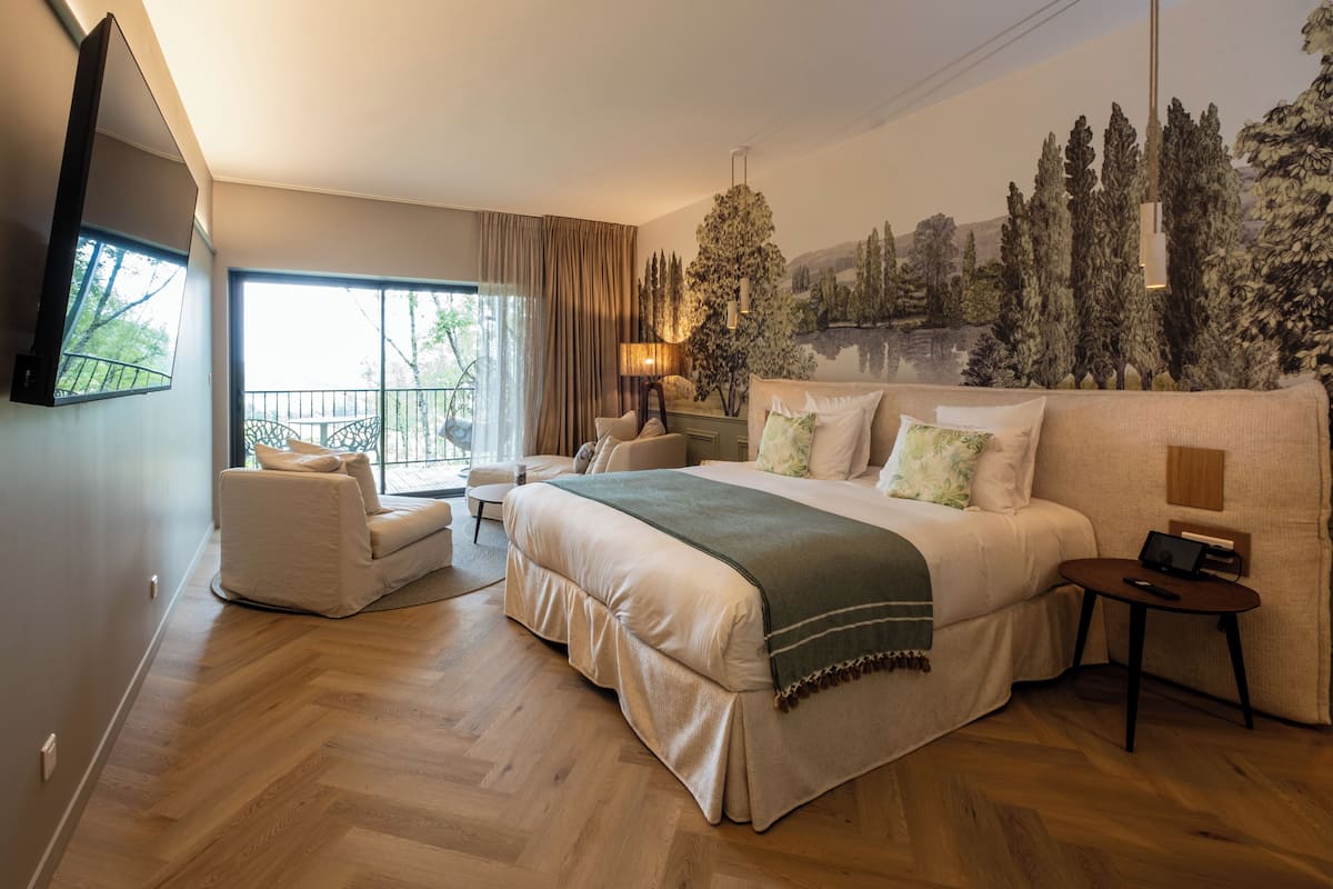 A bedroom with a large bed, a sofa, a TV, and a window with curtains.