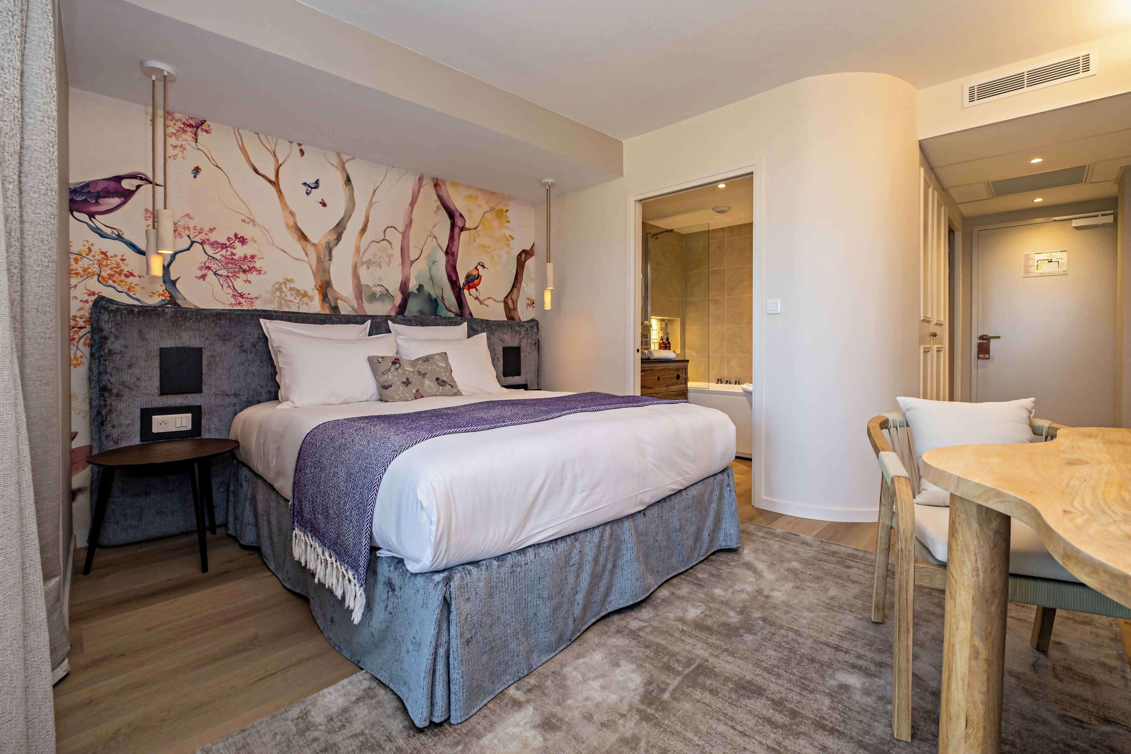 Un dormitorio moderno con una cama grande, una mesa de madera y un baño visible a través de una puerta abierta.