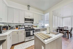 A modern kitchen with white cabinets, a microwave, stove, and a dining area with a table and chairs.