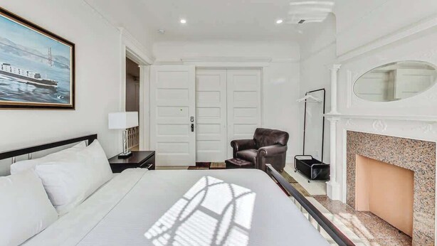 Een hotelkamer met een bed, een stoel, een open haard, een schilderij en een deur.