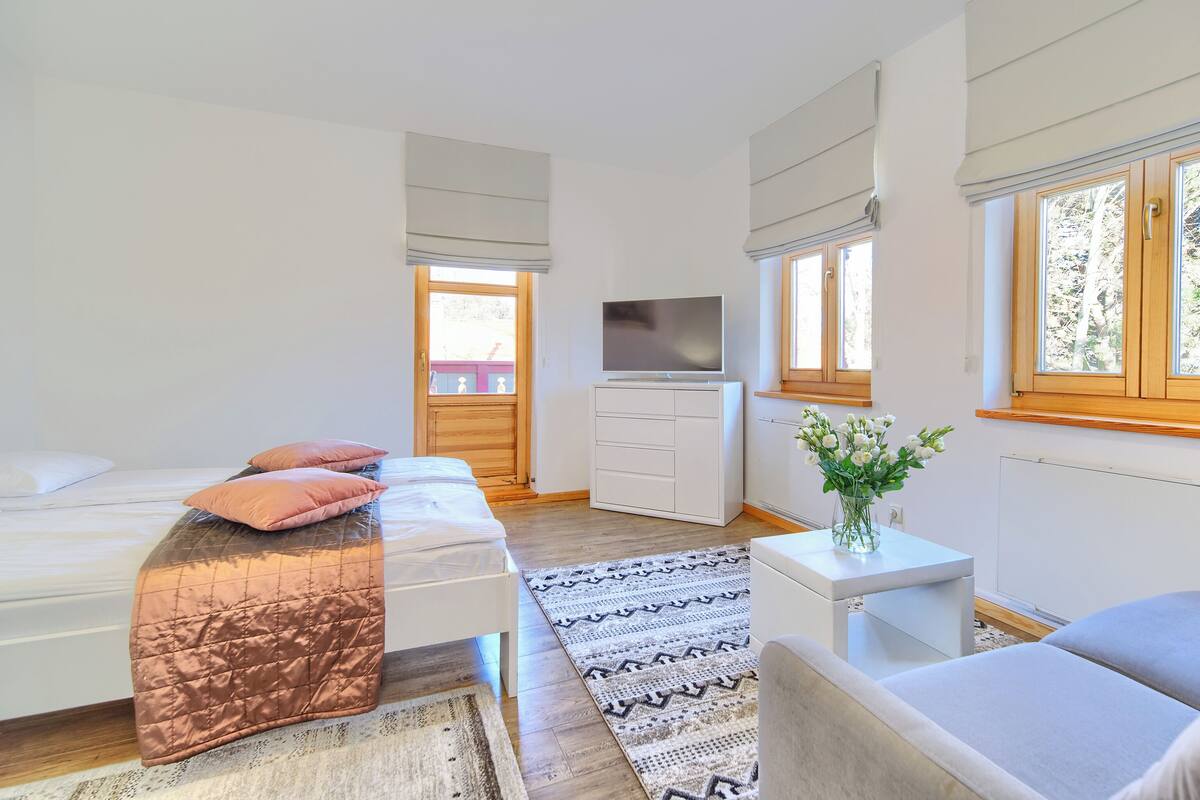 Un dormitorio moderno con una cama, un televisor, un escritorio y una ventana.