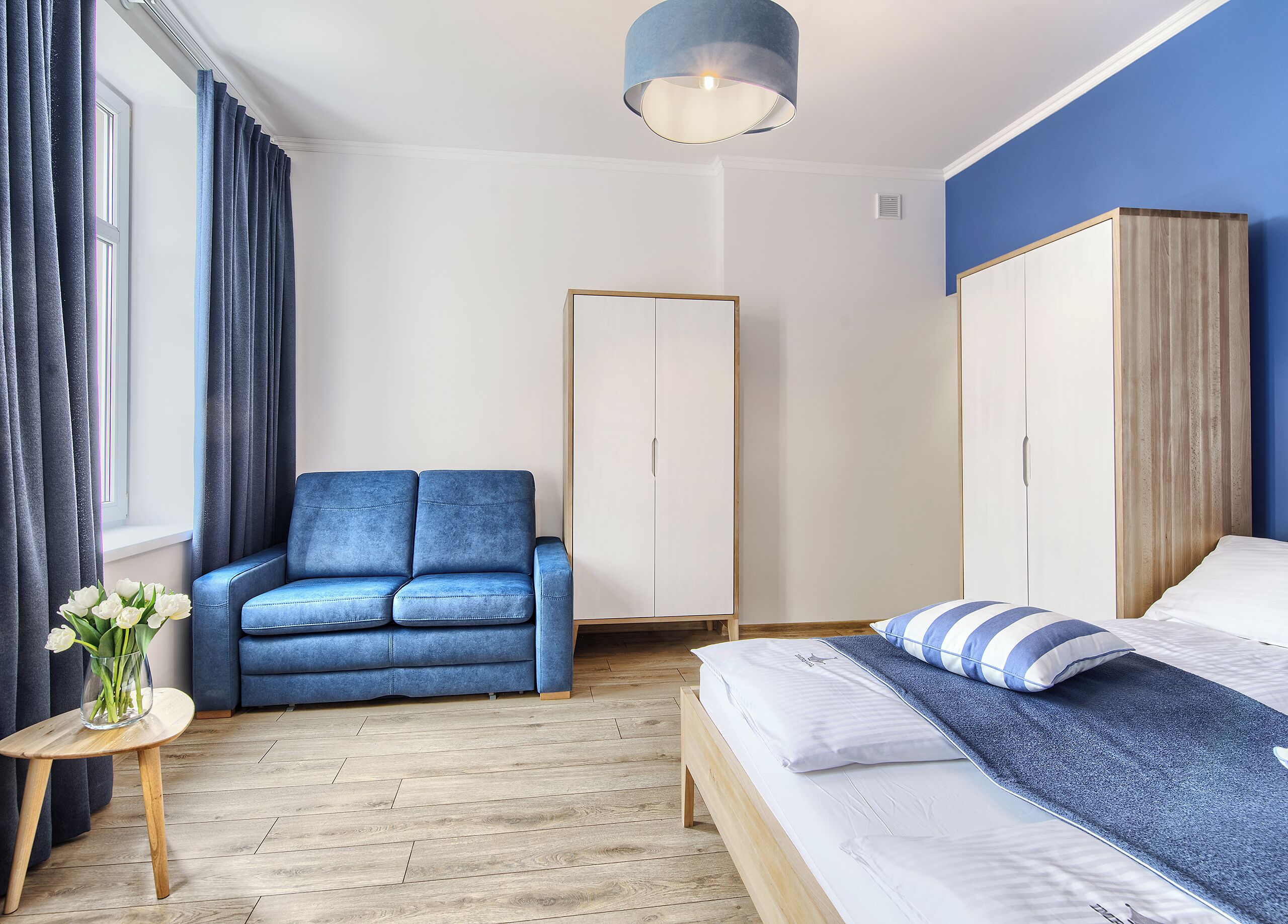 Quarto moderno com sofá azul, cama com travesseiro listrado e um guarda-roupa.