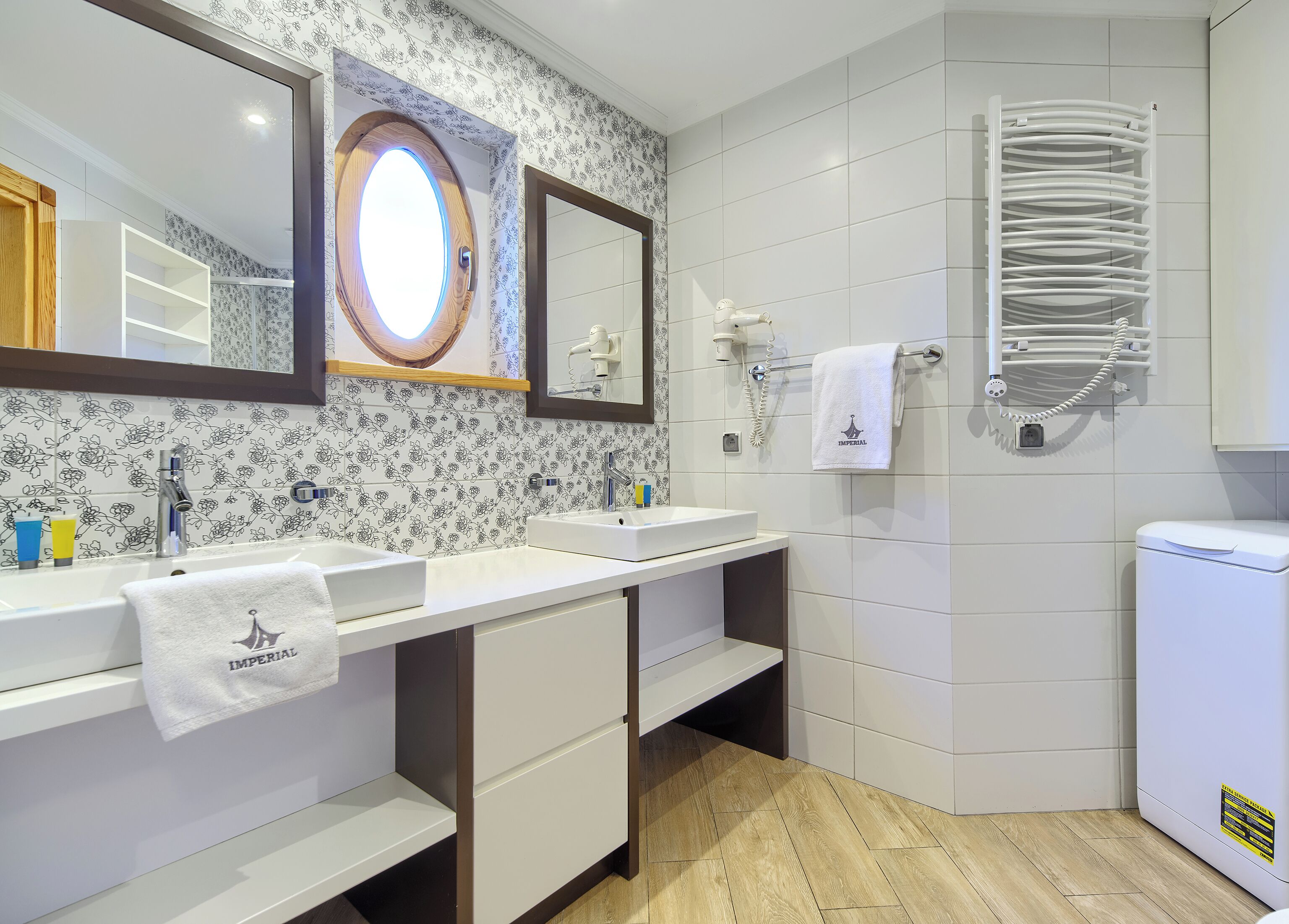 A modern bathroom with two sinks, a mirror, a towel rack, and a built-in heater.