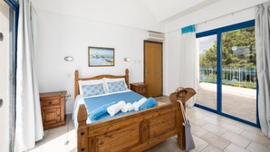 Ein Schlafzimmer mit einem hölzernen Bett, einem Nachttisch, einer Kommode und einem Balkon mit Blick auf Grünflächen.