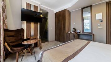 Une chambre d’hôtel moderne avec un grand lit, une chaise en bois, une petite table, un téléviseur et une armoire.