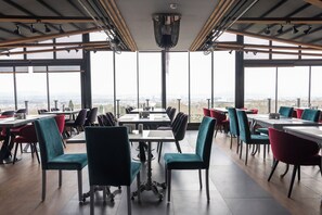 Un restaurante con mesas y sillas altas, ventanas amplias y vistas a la ciudad.