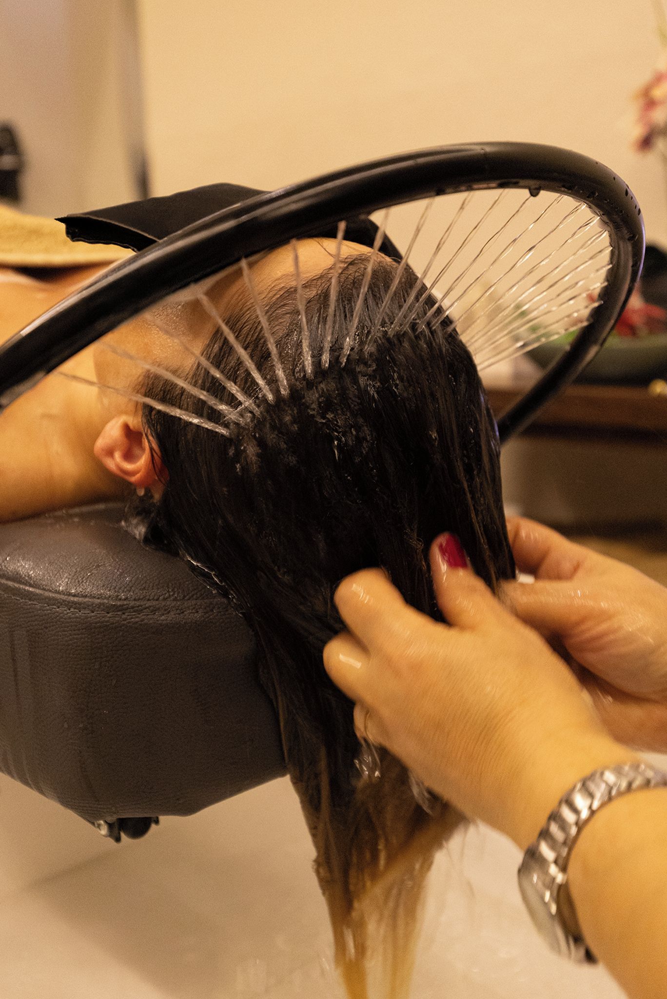 Una persona sentada en un sillón de salón con un secador de pelo colocado encima de la cabeza.