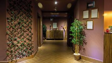 A hotel lobby with a wooden reception desk, a wall-mounted plant, and framed certificates on the wall.