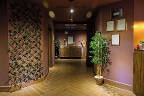 Un vestíbulo de hotel con un mostrador de recepción de madera, una planta suspendida en la pared y certificados enmarcados.