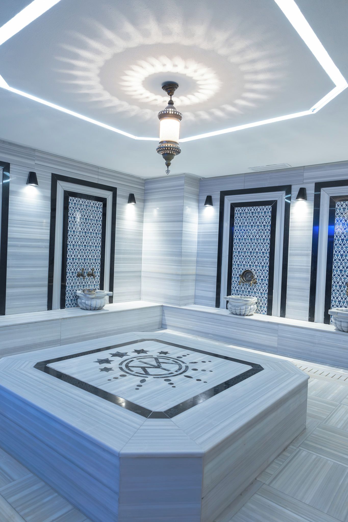 Un baño moderno con una bañera rectangular central, luces decorativas en el techo y baldosas de pared estampadas.