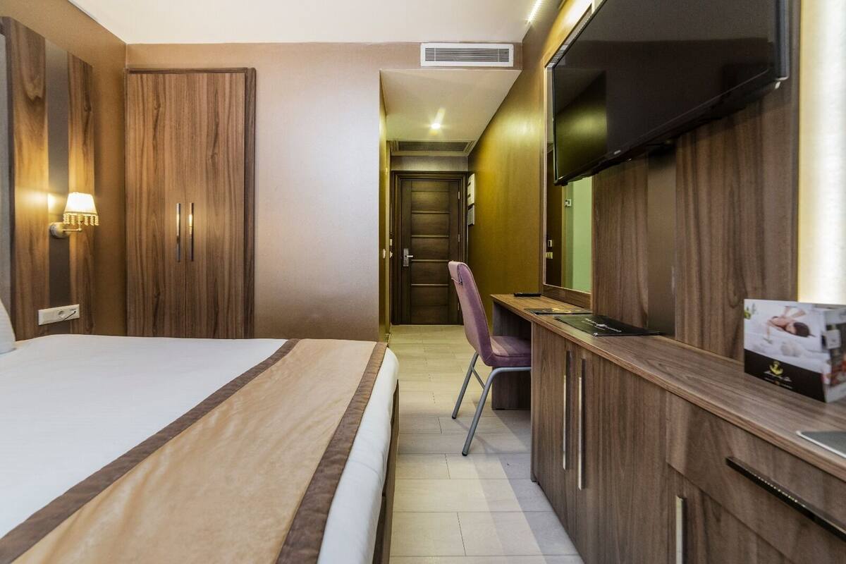 A hotel room with a bed, a desk, a chair, a TV, and a minibar.