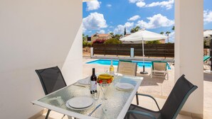 Una mesa de vidrio con platos, vino y un frutero, con vistas a una piscina y un área de estar exterior.