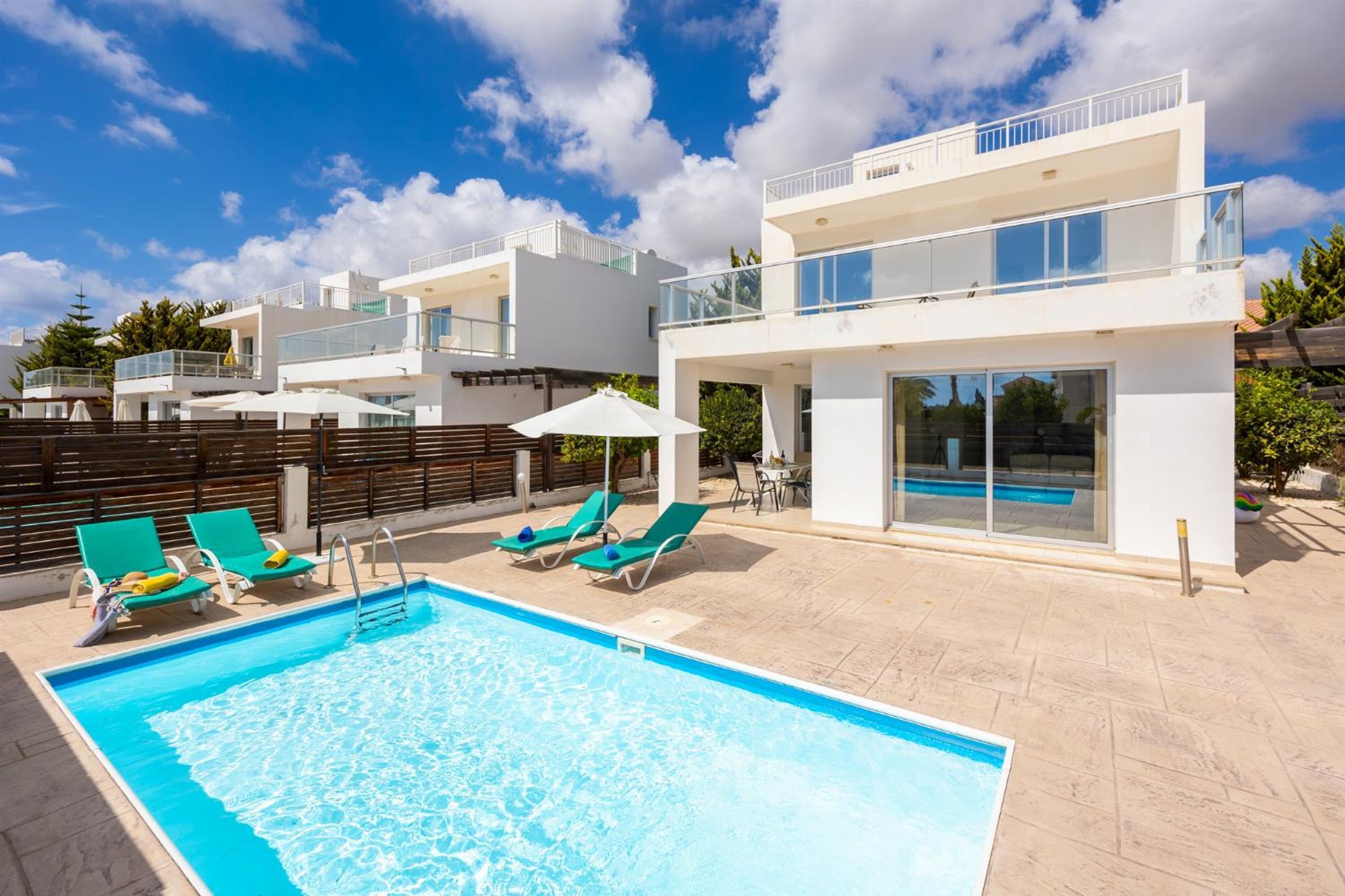 A modern two-story building with a swimming pool, outdoor seating, and a clear blue sky.