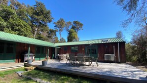 A rustic cabin with a green metal roof, a patio with wooden furniture, and a stone pathway leading to the entrance. - Close to the river, 11 TeAho  is 
a family lodge with plenty of character  (Tūrangi)