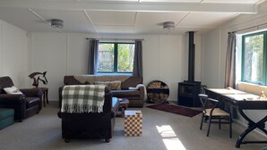 A cozy living room with a sofa, armchairs, a coffee table, a fireplace, and a large window. - Close to the river, 11 TeAho  is 
a family lodge with plenty of character  (Tūrangi)