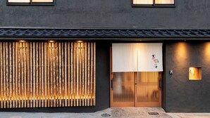 Facciata di un edificio con esterno scuro, ingresso in legno a listelli e tradizionale schermo giapponese shoji.