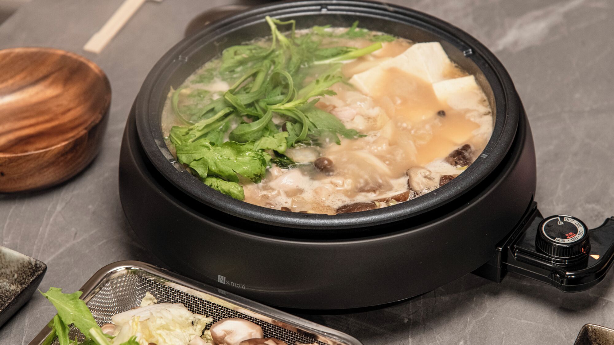 A hot pot with various ingredients like leafy greens and tofu, placed on a stove.