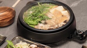 A hot pot with various ingredients like leafy greens and tofu, placed on a stove. - Harukazesou Tengatyaya (Osaka)