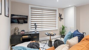Un dormitorio moderno con cama, televisor, cómoda, ventana con persianas y planta en maceta.