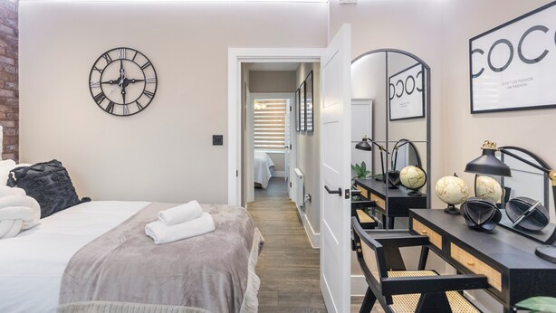 Un dormitorio moderno con una cama, un reloj, un escritorio con un espejo y un cartel enmarcado en la pared.