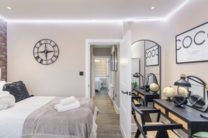 Una camera da letto moderna con un letto, una sveglia, una scrivania con uno specchio e un cartello appeso al muro.