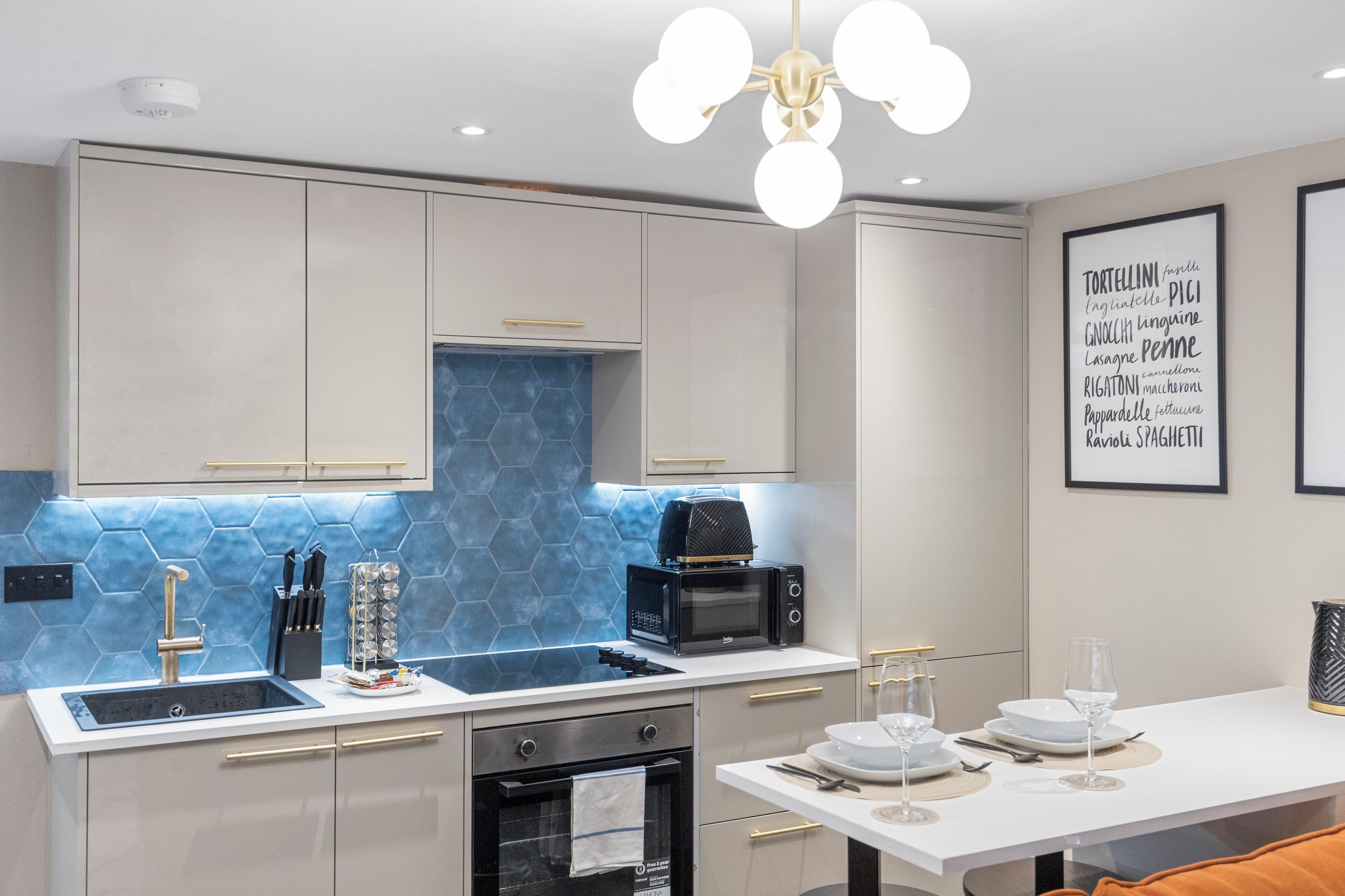 A modern kitchen with a built-in stove, a microwave, and a sink. There is a dining table with plates and glasses set up for a meal.