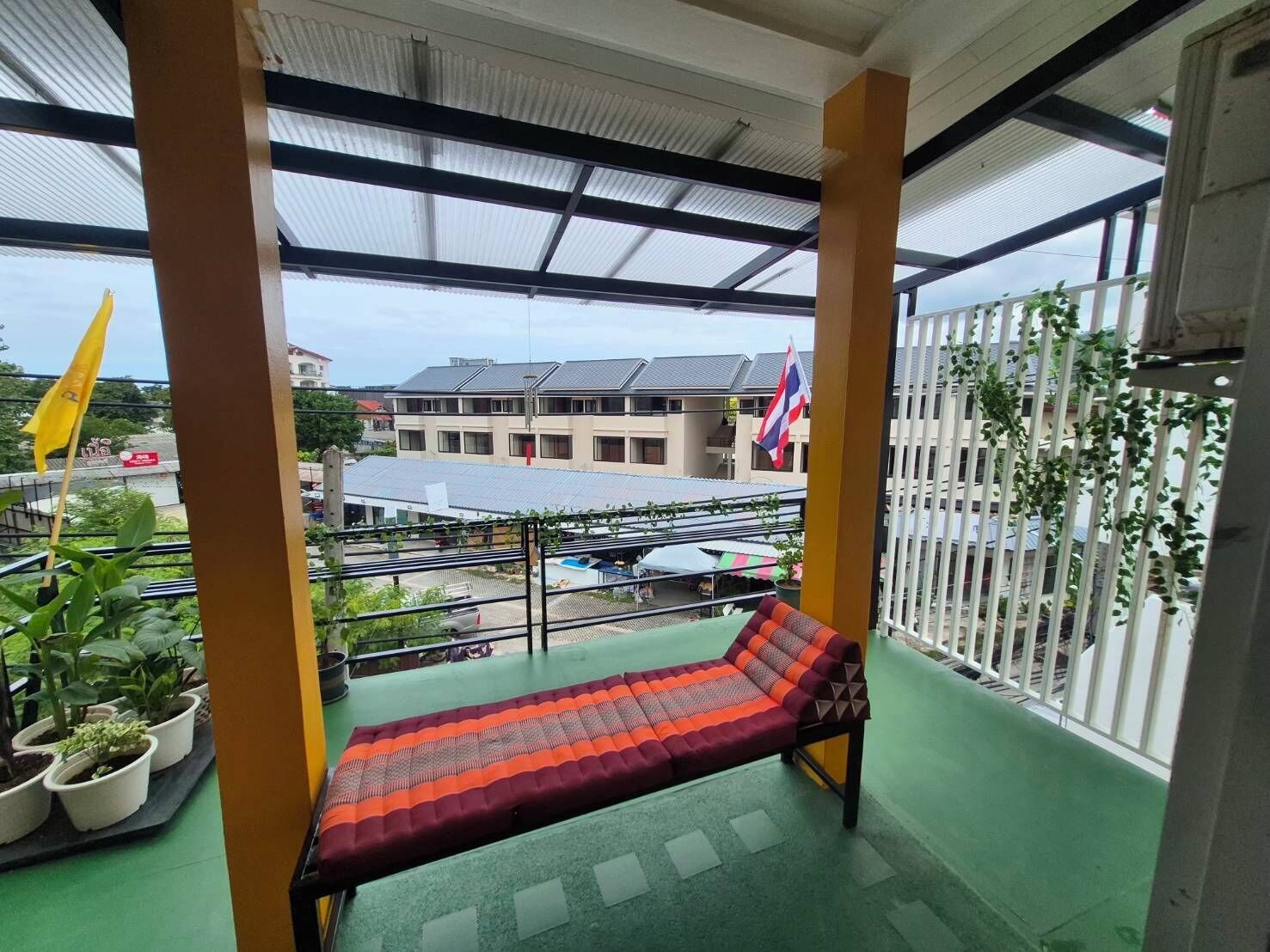 A balcony with a bench, potted plants, and a view of buildings and flags.