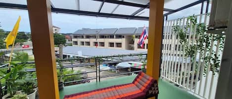 A balcony with a bench, potted plants, and a view of buildings and flags.