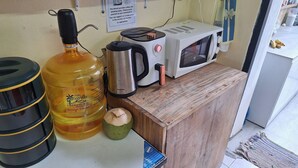 Une petite cuisine équipée d’un grand distributeur d’eau, d’une machine à café, d’un four à micro-ondes et d’un petit placard.