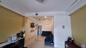 Un espace d’accueil comprenant un guichet pour les billets, un téléviseur fixé au mur et un canapé de couleur sombre à l’arrière-plan.