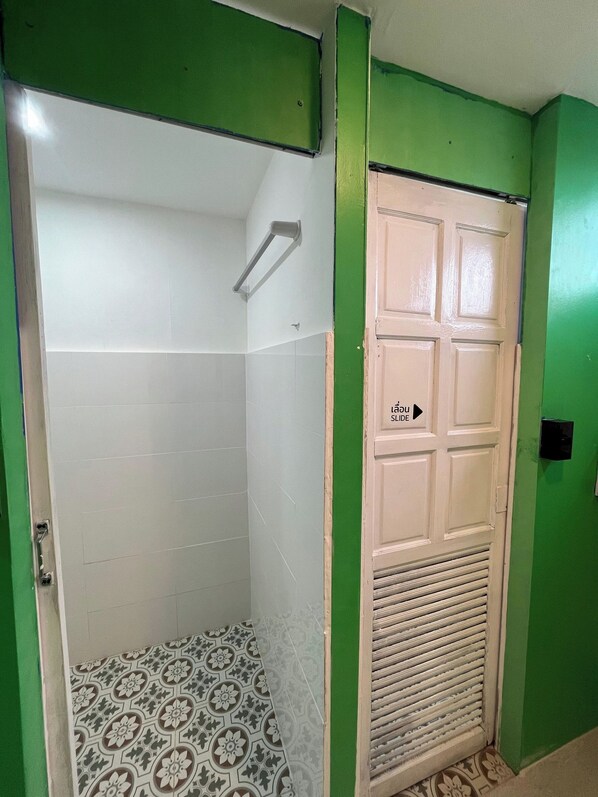 A bathroom with a shower, a toilet, and a door with a sign indicating the direction to the slide. - DK1 Hostel (Koh Samui)