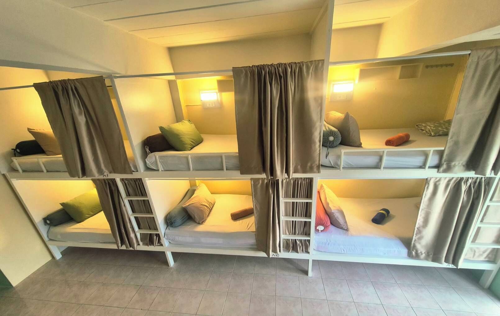 A dormitory-style room with bunk beds, each with a pillow and a blanket.