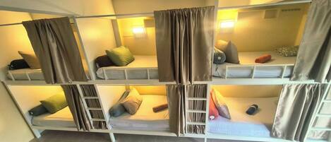 A dormitory-style room with bunk beds, each with a pillow and a blanket.