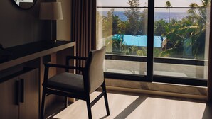 Habitación de hotel con escritorio, silla y un amplio ventanal con vistas a una piscina y zonas verdes.