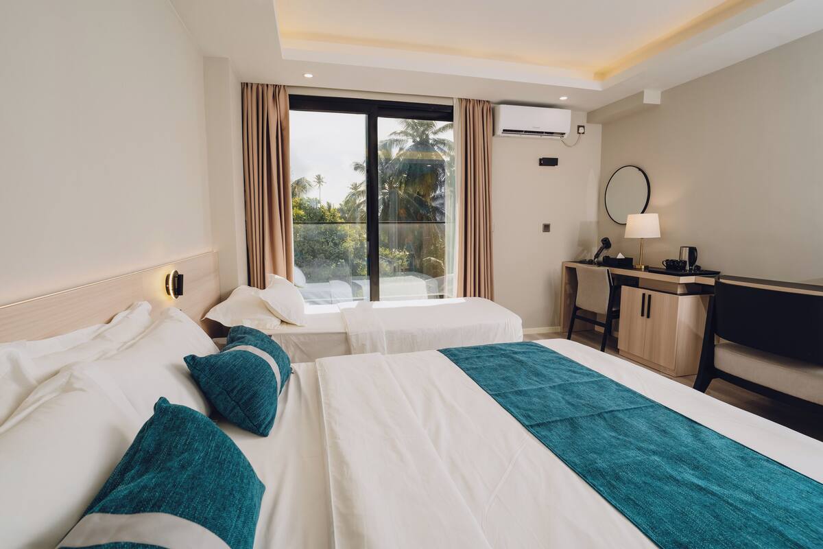 Een hotelkamer met twee bedden, een bureau, een stoel, een raam met gordijnen en een airconditioning.