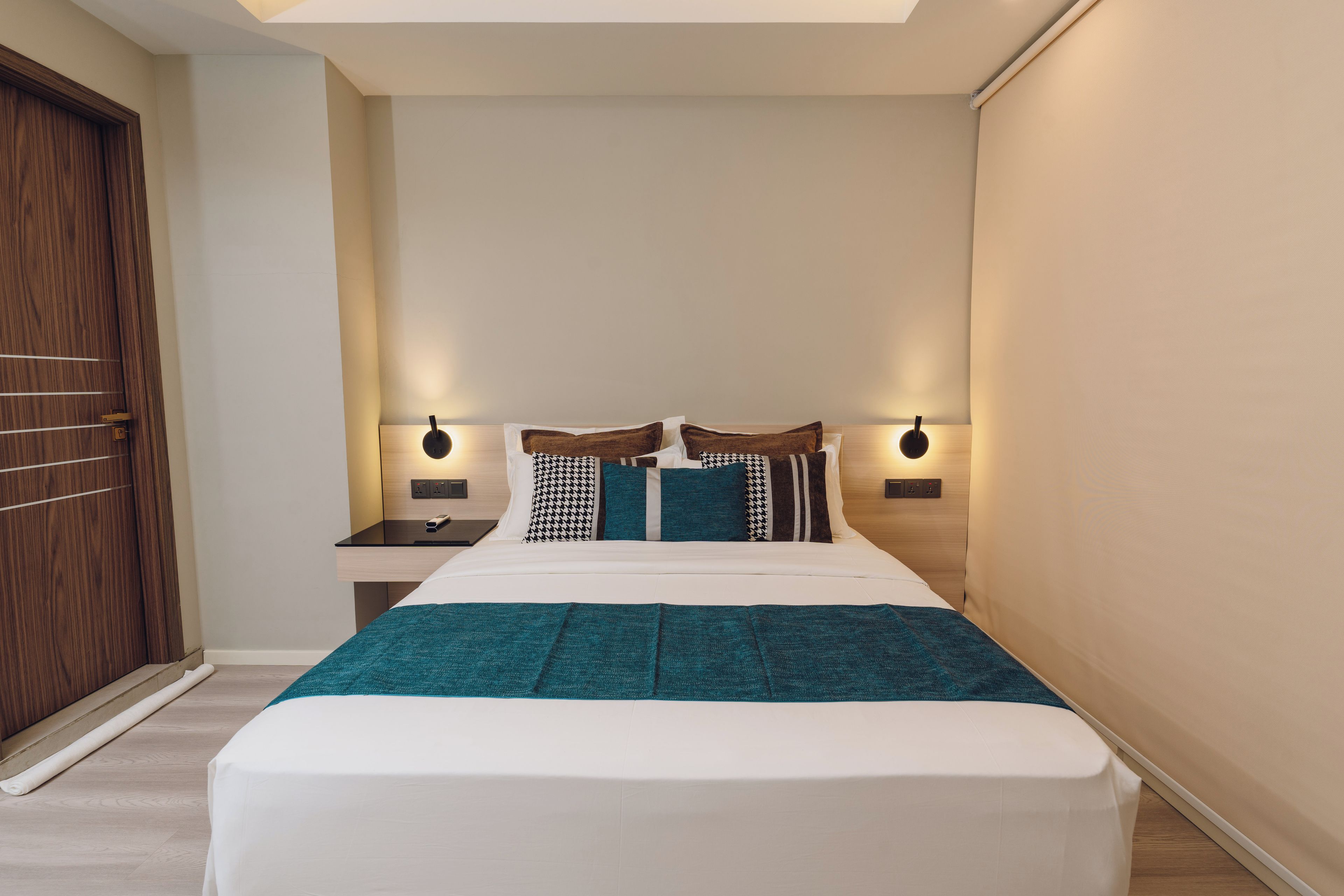 A hotel room with a bed, bedside tables, a nightstand, a wooden door, and a ceiling light.