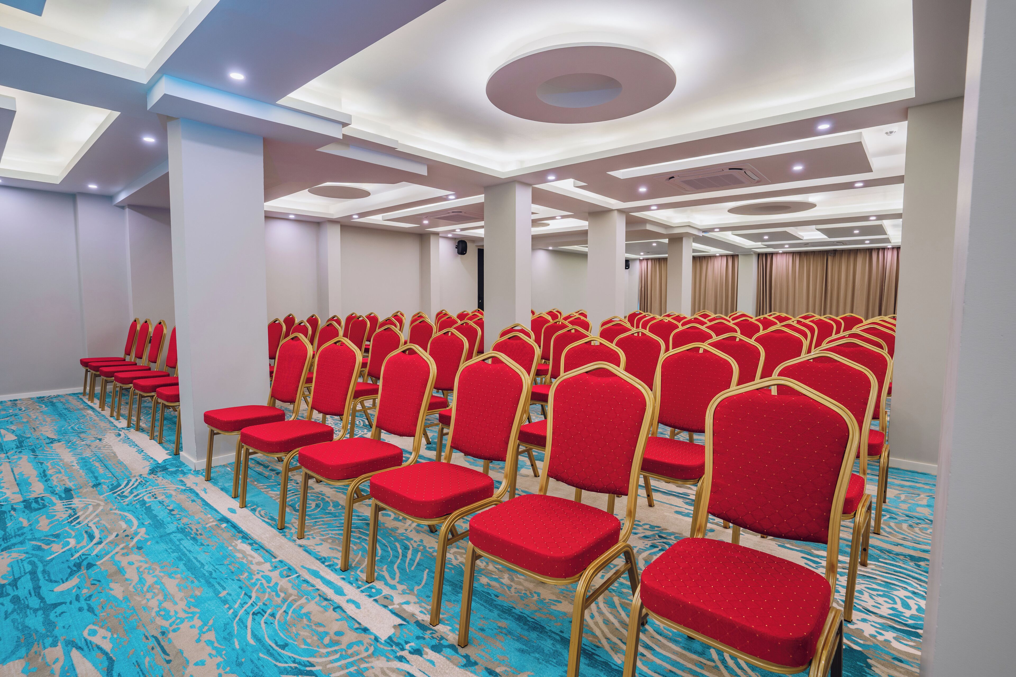 A conference room with rows of red chairs and a blue patterned carpet.