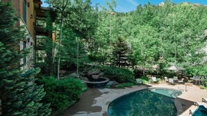 Una piscina rodeada de abundante vegetación y un deck de piedra.