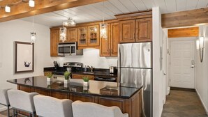 Una cocina moderna con armarios de madera, electrodomésticos de acero inoxidable, una isla central con taburetes y luminarias colgantes.