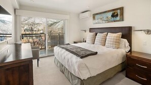 A bedroom with a large bed, a desk, and a view of a snowy landscape through a sliding glass door. - 3 Bedroom Gold-rated Condo at the Base of Aspen Mountain (Aspen)