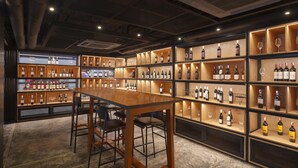A bar area with multiple shelves of wine bottles and glasses, a wooden bar counter, and bar stools. - Radisson RED Phuket Patong Beach (Patong)