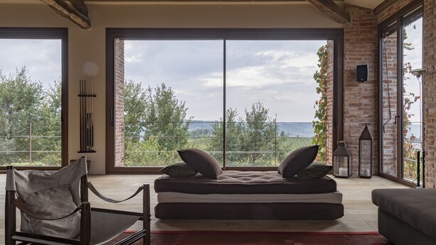 Een moderne kamer met een grote schuifglasdeur die uitkomt op een balkon, een hangstoel, een bank en een klein tafeltje met een kaars.