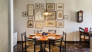 Een eetkamer met een ronde tafel voor zes personen, omringd door stoelen, met lijstwerken aan de muur en een vintage klok.