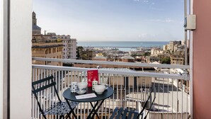 Een balkon met een tafel gedekt voor twee, met uitzicht op een stadslandschap met gebouwen en de zee.