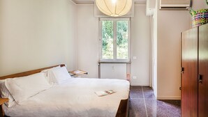 Hotelkamer met een bed, een raam met uitzicht op groen, een airconditioner en een houten garderobe.