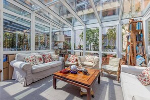 A sunlit room with a glass ceiling, furnished with sofas and a coffee table, and a bookshelf filled with books. - Noisette house with garden (Milano)
