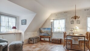 A cozy room with a dining table, chairs, a sofa, and a window with curtains. - Green Teft - thatched house in the southwest part of the village of Keitum (Sylt / OT Keitum)
